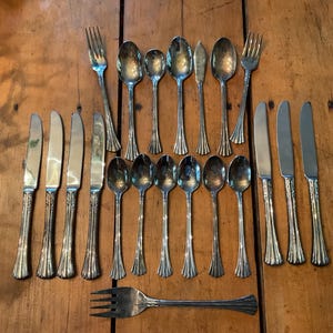 May include: A collection of vintage silverware, including forks, knives, and spoons, arranged on a wooden surface. The silverware has ornate handles and a shiny, reflective surface, suggesting a formal dining setting.