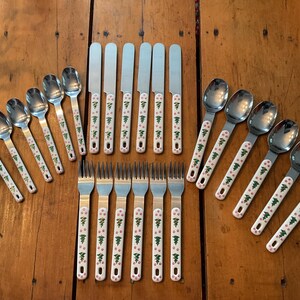 May include: A vintage flatware set with stainless steel blades and bowls, and white handles decorated with green trees and pink dots. The set includes spoons, forks, and knives, arranged on a wooden surface.