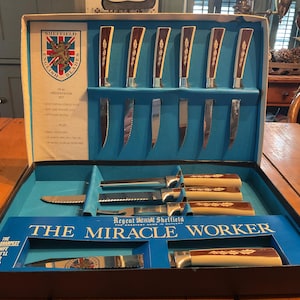 May include: A vintage Sheffield English Blades knife set in a presentation box. The set includes knives with brown and cream handles, and silver blades. The box is blue and white with the text "THE MIRACLE WORKER".