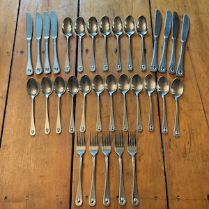 May include: A collection of stainless steel flatware consisting of four dinner knives, eight soup spoons, eleven teaspoons, and five dinner forks. Each piece features a simple, smooth handle design with a rounded end and a polished finish.