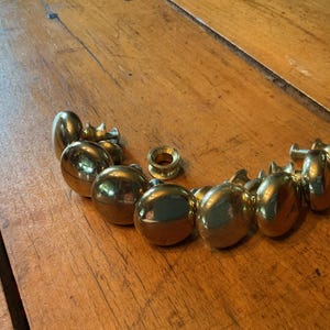 May include: A collection of polished brass cabinet knobs with a smooth, rounded profile. Each knob features a reflective metallic finish and includes a threaded metal screw attachment for installation, arranged in a curved formation.