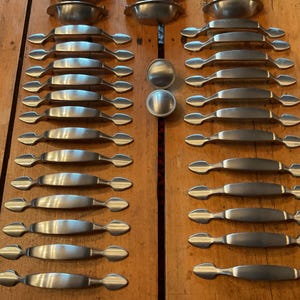 May include: A collection of brushed nickel cabinet hardware, including handles and knobs, arranged on a wooden surface. The handles are approximately 6 inches long. The hardware is designed for kitchen or bathroom cabinets.