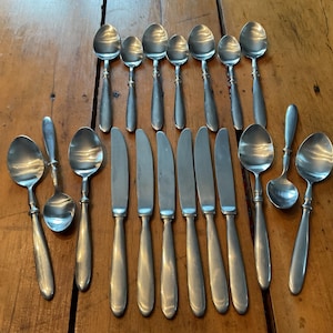 Peut inclure: Un ensemble de couverts anciens, comprenant des cuillères et des couteaux, disposés sur une surface en bois. Les cuillères ont des cuillères arrondies et des manches ornés. Les couteaux ont un design simple et élégant. Les couverts sont probablement en argent ou en métal argenté.