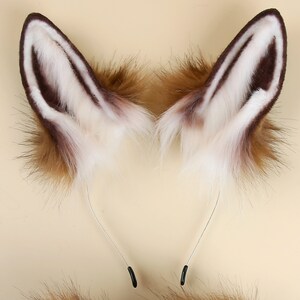 May include: A pair of brown and white faux fur fox ears with a silver headband. The ears are attached to the headband with black clips.