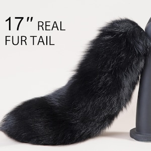 Può includere: Una coda di pelliccia vera nera lunga 43 cm. La coda è attaccata a una mano di manichino ed è esposta su un supporto nero.