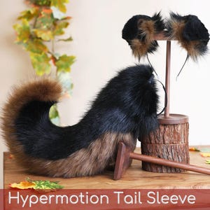 May include: A faux fur tail and a pair of matching animal ears on a headband. The tail is black and brown with a curved shape. The ears are black and brown with long, fluffy fur. The text "Hypermotion Tail Sleeve" is visible at the bottom.