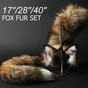 Può includere: Un set di tre code di volpe in pelliccia marrone, nera e bianca. Le code sono lunghe 43 cm, 71 cm e 102 cm. Le code sono esposte su un supporto in metallo. Il testo "17"/"28"/"40" FOX FUR SET" è visibile nell'immagine.