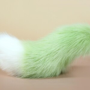 May include: A fluffy green and white faux fur tail. The tail is long and bushy, with a white tip and a green base.