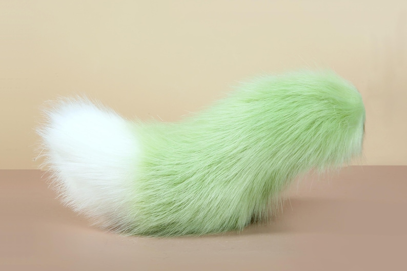 May include: A fluffy green and white faux fur tail. The tail is long and bushy, with a white tip and a green base.