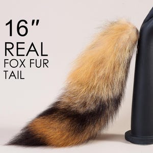 Può includere: Una coda di volpe in vera pelliccia di 40,6 cm. La coda è marrone, nera e arancione ed è esposta su un supporto nero.