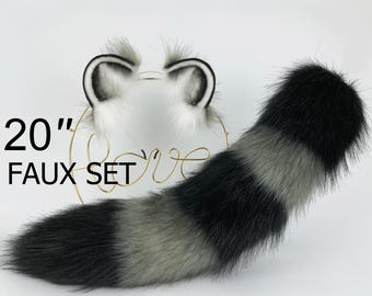 Può includere: Un set di coda e orecchie in pelliccia sintetica da 50 cm con una coda a strisce nere e grigie e un paio di orecchie in pelliccia bianca con punte nere.