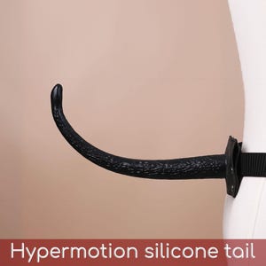 May include: A black silicone tail with a textured surface attached to a black nylon belt. The tail curves upward and is secured to the belt by a black mounting piece. The text "Hypermotion silicone tail" is printed at the bottom.