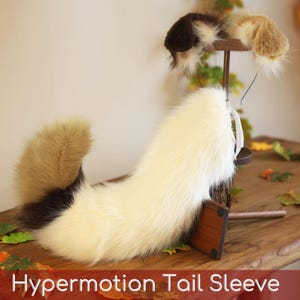 May include: A faux fur animal tail and matching ear headband set featuring a tri-color pattern of cream, tan, and dark brown. The tail is long and fluffy with a curved shape, while the ears are rounded and fuzzy. Text reads: Hypermotion Tail Sleeve.