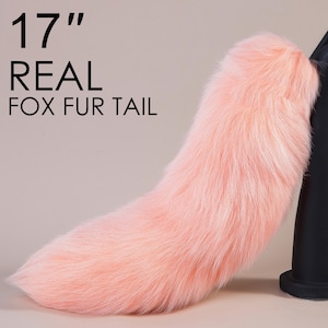 Può includere: Una coda di volpe in vera pelliccia di colore rosa chiaro, lunga 43 cm. La coda è esposta su un supporto nero.