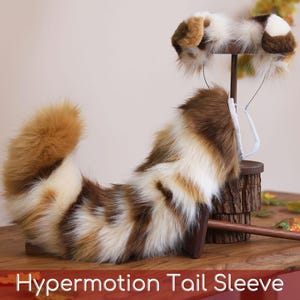 May include: A faux fur animal tail and matching ear headband set featuring a multi-colored pattern of brown, tan, and white long-pile synthetic fibers. The tail is curved and the ears are mounted on a thin wire frame. Text reads: Hypermotion Tail Sleeve.
