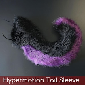 Puede incluir: Una funda de cola de piel sintética con un diseño curvo, pelo largo negro en la parte superior y pelo morado vibrante en la parte inferior. El accesorio incluye dos bucles de sujeción negros en la base y muestra el texto Hypermotion Tail Sleeve.