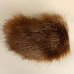 May include: A brown faux fur tail with long, soft fibers. The tail is fluffy and appears to be made of high-quality material.
