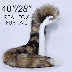 Può includere: Una coda di volpe in pelliccia vera di 40 pollici per 28 pollici. La coda è marrone, nera e bianca con una punta soffice. La coda è esposta su una mano di manichino bianca.