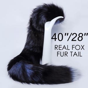 Può includere: Una lunga coda di volpe in pelliccia nera e argento, che misura 101,6 cm di lunghezza e 71,1 cm di circonferenza. La coda è esposta su un manichino bianco. "REAL FOX FUR TAIL" è scritto in nero sotto la coda.