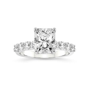 K&ouml;nnte beinhalten: Ein quadratischer Diamantring mit Pav&eacute;-Fassung. Der Ring hat eine silberne Band und einen gro&szlig;en, klaren Mittel-Stein.
