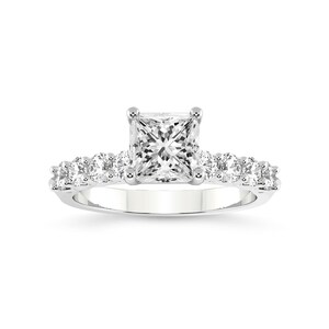 K&ouml;nnte beinhalten: Ein silberner Verlobungsring mit einem quadratischen Diamanten in der Mitte und einer Reihe kleinerer Diamanten.
