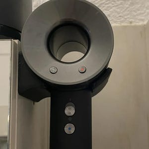 May include: A black hair dryer with a round nozzle and three buttons. The buttons are labeled with icons. The dryer is mounted on a wall.