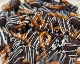 May include: A close-up shot of chocolate-covered pretzels. The pretzels are dipped in dark chocolate and drizzled with white chocolate. The pretzels are a mix of shapes and sizes, with some covered entirely in chocolate and others partially dipped.