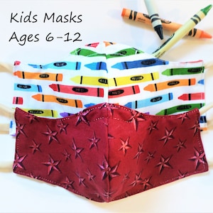 K&ouml;nnte beinhalten: Zwei Kindermasken, eine mit rotem Hintergrund und wei&szlig;en Sternen, die andere mit wei&szlig;em Hintergrund und bunten Buntstiften. Der Text "Kids Masks Ages 6-12" befindet sich &uuml;ber den Masken.