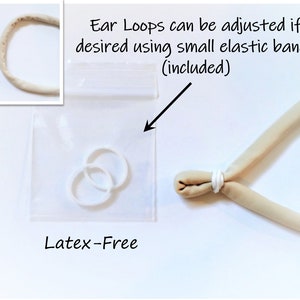 K&ouml;nnte beinhalten: Zwei wei&szlig;e latexfreie Gummib&auml;nder in einem durchsichtigen Plastikbeutel. Die B&auml;nder k&ouml;nnen verwendet werden, um die Ohrschlaufen einer Gesichtsmaske anzupassen. Der Text "Ear Loops can be adjusted if desired using small elastic bands (included)" steht &uuml;ber dem Beutel.