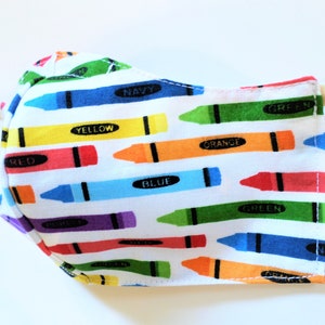 K&ouml;nnte beinhalten: Eine wei&szlig;e Gesichtsmaske mit einem bunten Kreidonsmuster. Die Kreidons sind diagonal angeordnet und haben die W&ouml;rter "rot", "gelb", "orange", "gr&uuml;n", "blau" und "marine" darauf geschrieben.