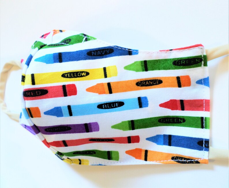 K&ouml;nnte beinhalten: Eine wei&szlig;e Gesichtsmaske mit einem bunten Kreidonsmuster. Die Kreidons sind diagonal angeordnet und haben die W&ouml;rter "rot", "gelb", "orange", "gr&uuml;n", "blau" und "marine" darauf geschrieben.
