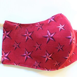 K&ouml;nnte beinhalten: Eine rote Gesichtsmaske mit einem wei&szlig;en Sternenmuster. Die Maske ist aus Stoff und hat ein wei&szlig;es Gummiband.