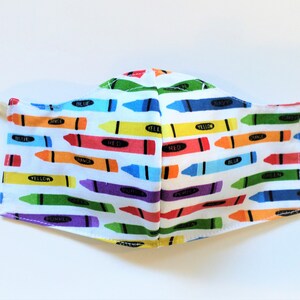 K&ouml;nnte beinhalten: Eine wei&szlig;e Gesichtsmaske mit einem bunten Kreid Muster. Die Kreiden sind horizontal angeordnet und mit ihren Farben beschriftet, darunter Rot, Orange, Gelb, Gr&uuml;n, Blau, Lila und Schwarz.