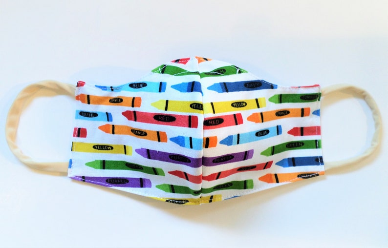 K&ouml;nnte beinhalten: Eine wei&szlig;e Gesichtsmaske mit einem bunten Kreid Muster. Die Kreiden sind horizontal angeordnet und mit ihren Farben beschriftet, darunter Rot, Orange, Gelb, Gr&uuml;n, Blau, Lila und Schwarz.