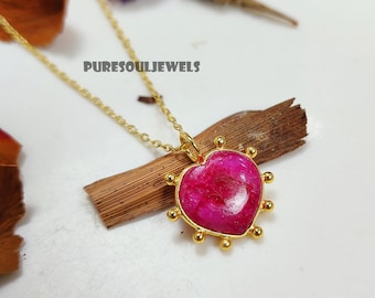 May include: A gold chain necklace with a pink heart-shaped pendant surrounded by gold beads. The pendant has a textured surface and is set against a wooden background. The text "PURESOULJEWELS" is visible in the image.