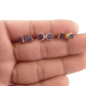 Peut inclure: Un ensemble de quatre boucles d'oreilles en pierre précieuse de rubis brut avec des montures en or et en argent. Les boucles d'oreilles sont présentées sur une main.