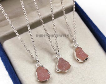 May include: Three silver necklaces with raw, pink gemstones. The pendants are irregularly shaped and set in silver. The necklaces are displayed in a blue velvet box. The text "PURESOULJEWELS" is visible in the background.