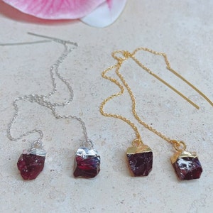 May include: Two pairs of dangle earrings with raw garnet stones. One pair has silver chains and the other has gold chains.