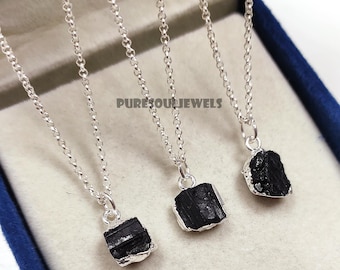 Peut inclure: Trois colliers en argent avec des pendentifs en tourmaline noire. Chaque collier présente une chaîne délicate et une pierre noire brute de forme irrégulière. Les pendentifs sont sertis d'argent. L'image est sur fond clair.