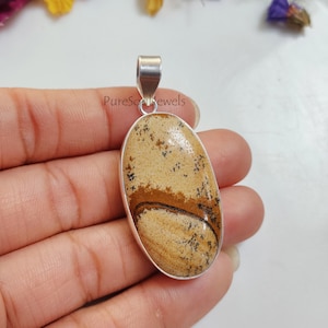 Op de afbeelding: Een zilveren hanger met een ovale steen in bruin en beige met een swirl-patroon. De steen is gezet in een zilveren bezel en heeft een zilveren bail.
