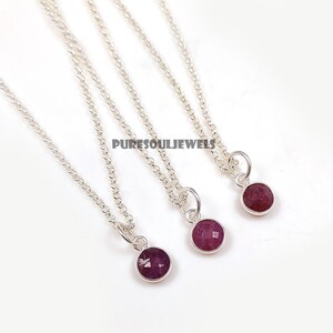 May include: Three silver necklaces with small, round, faceted, deep red gemstones. The necklaces have delicate silver chains and are displayed against a white background. The text "PURESOULJEWELS" is visible in the image.