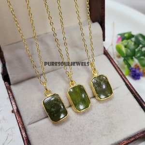 May include: Three gold chains with green gemstone pendants. Each pendant is a rectangular shape with a gold border. The chains are displayed in a brown box.