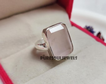 May include: A silver ring with a large, rectangular, light pink gemstone. The ring is in a red velvet box. The text "PURESOUL JEWELS" is visible on the bottom of the image.
