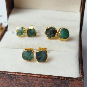 May include: A pair of emerald green gemstone earrings with gold settings. The earrings are displayed in a brown jewelry box. The text "PureSoulJewels" is visible in the image.