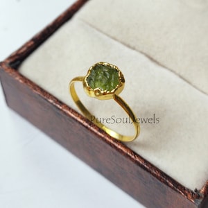 May include: A gold ring with a green peridot gemstone. The ring is in a brown box with the text "PureSoulJewels".