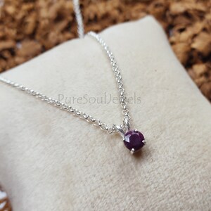 May include: A silver chain necklace with a small, round, dark purple gemstone pendant.