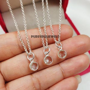 Op de afbeelding: Drie delicate zilveren kettingen met kleine, ronde, facetgeslepen, lichtgroene edelstenen. De kettingen worden op een hand getoond, met de tekst "PURESOULJEWELS" zichtbaar op de achtergrond. De kettingen zitten in een rode sieradendoos.