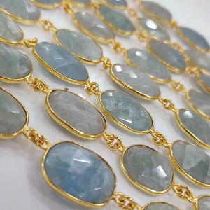 May include: A gold chain necklace featuring multiple faceted, oval-shaped light blue gemstones set in individual gold bezels. The stones are arranged in a repeating pattern, connected by small gold links, creating a continuous decorative strand.