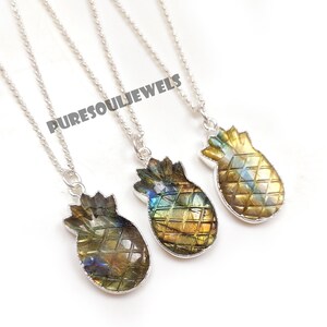 May include: Three silver necklaces with pineapple-shaped pendants. The pendants are made of a gemstone with a mix of yellow, green, and blue hues. The necklaces are displayed on a white surface. The text "PURESOULJEWELS" is visible.
