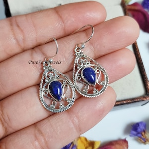 Puede incluir: Pendientes de plata de ley con un diseño en forma de lágrima que presenta una piedra preciosa de lapislázuli azul. Los pendientes tienen intrincados detalles de filigrana.